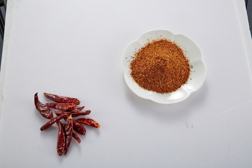 Dried chili pepper and chili powder on white table
