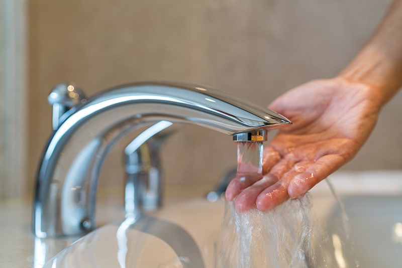 Woman taking a bath at home checking temperature touching running water with hand