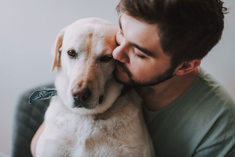 a bearded man kissing his dog while enjoying rest together