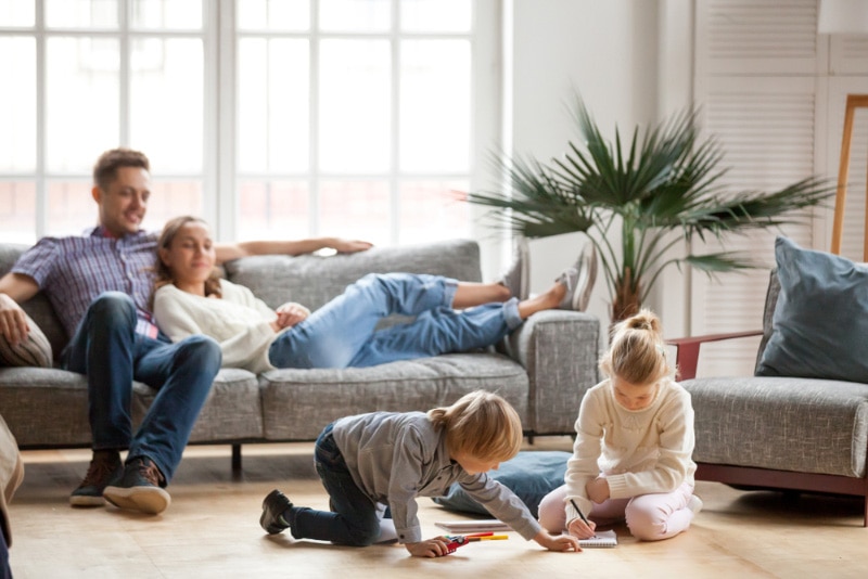 children drawing together on the floor and parents relaxing on the couch at home