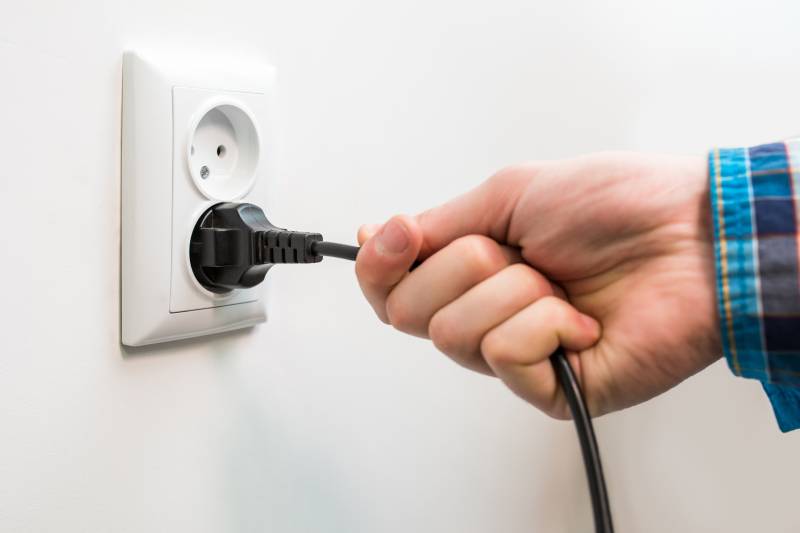 male hand is pulling an electrical cord plugged into a socket