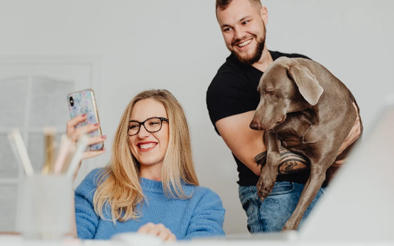 man and woman looking at their phone with their dog