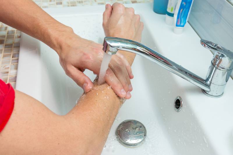 man washes his hands up to the elbows under the tap