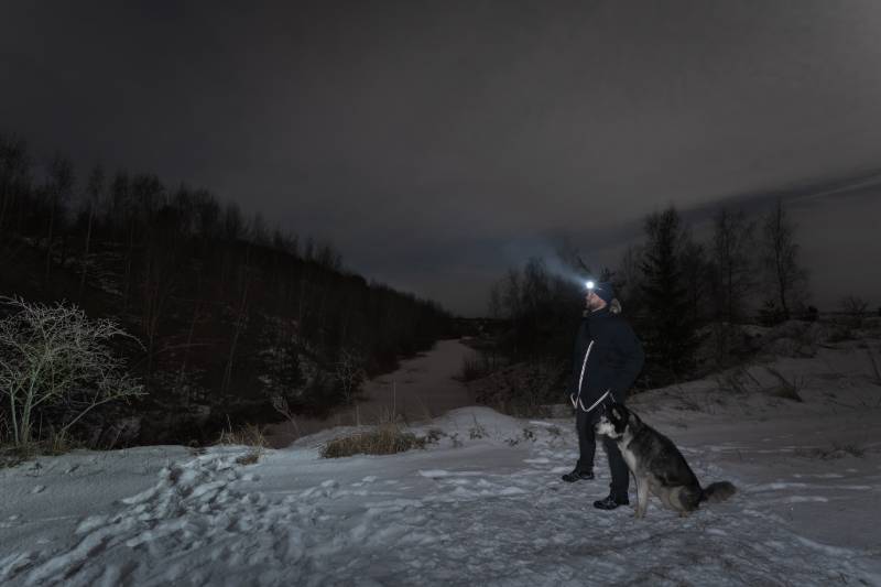 man with a headlamp walks with a husky dog