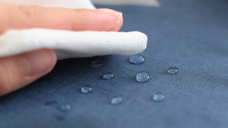 person wiping water droplets from surface of waterproof fabric