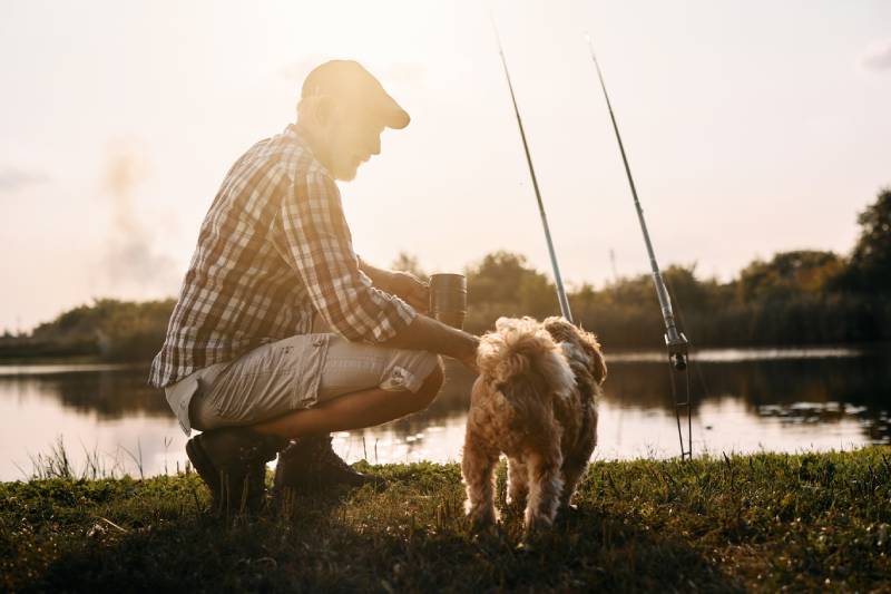 senior man enjoying with his dog while fishing on the river at sunset