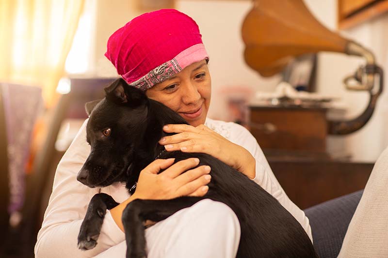 woman hugging her pet, and with pink scarf on her head due to breast cancer