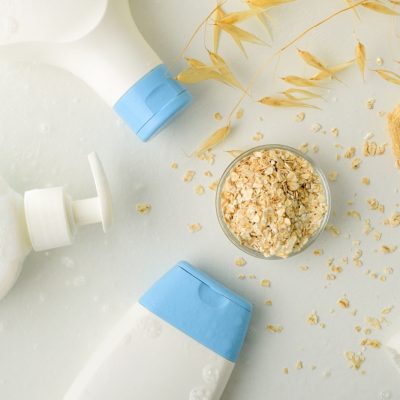 Detail of bath products with oat extract with straws and flakes on white table