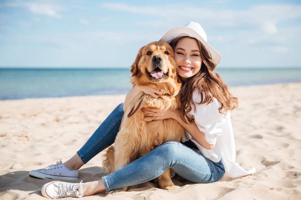 woman-and-her-dog-sitting-on-the-sand